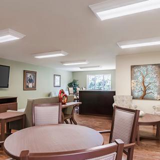 A cozy interior space with tables and chairs arranged for dining, featuring wall decor and ample lighting.