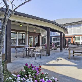 A cozy outdoor patio area with tables, chairs, and colorful flowers, adjacent to a modern building.
