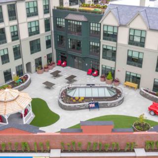 A modern apartment complex featuring a courtyard with a pool, seating areas, and a gazebo.