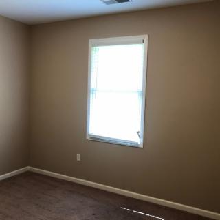 An empty room with beige walls and a single window letting in natural light.