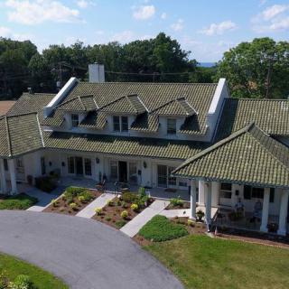 A large colonial-style house with a green roof and neatly arranged landscaping.
