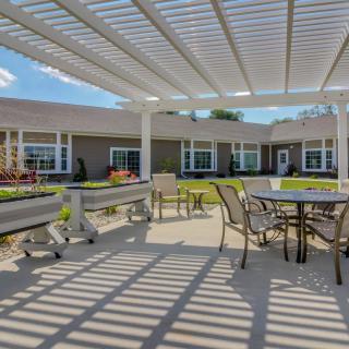A sunny outdoor patio with a pergola providing shade over tables and chairs.