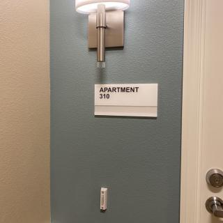 A sign for apartment 316 is mounted on the wall next to a door, illuminated by a wall-mounted light.