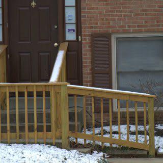 A snowy wooden ramp leads to the door of a brick building.