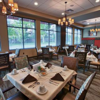 A spacious and elegantly decorated restaurant dining room with neatly set tables and large windows.