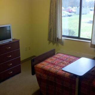 A small room with a single bed, television, and a window offering an outside view.