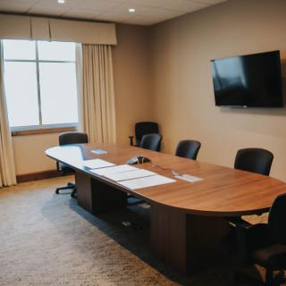 A modern conference room with a wooden table, several chairs, and a wall-mounted television.