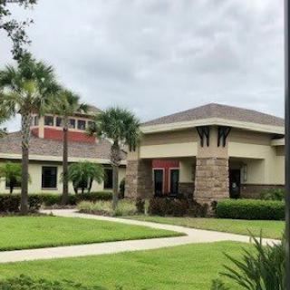 A modern building surrounded by a well-maintained landscape with trees and grass under a cloudy sky.