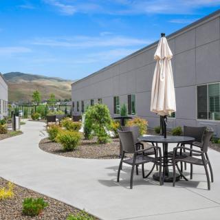 A peaceful outdoor patio area with tables, chairs, and umbrellas surrounded by landscaped gardens.