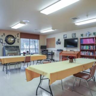 A classroom setup with tables and chairs, featuring a whiteboard, bookshelves, and wall decorations.