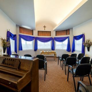 A small chapel with a piano, chairs, and blue curtains adorning the windows.