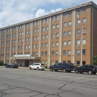 A multi-story brick building featuring several windows and a parking area in front.