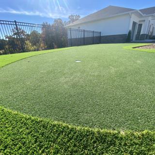A backyard putting green with artificial turf under a clear blue sky.