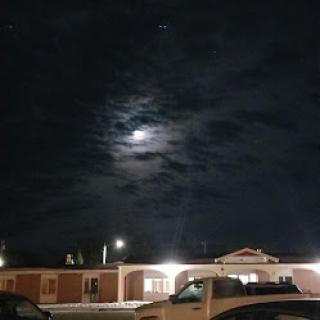 A serene night sky with the moon peeking through the clouds, illuminating nearby buildings.