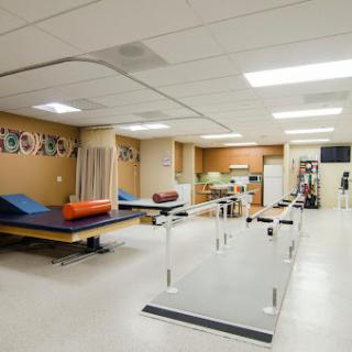 A spacious physical therapy room equipped with treatment tables and walking rails.