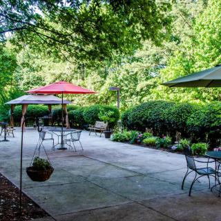 A peaceful outdoor patio area with tables, chairs, and umbrellas surrounded by lush greenery.