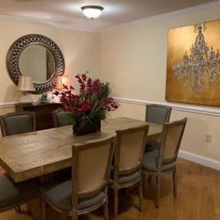 A cozy dining room with a large wooden table, surrounded by chairs, adorned with a floral centerpiece and complemented by wall art and a decorative mirror.