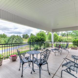 A covered patio with metal furniture overlooks a lush garden.
