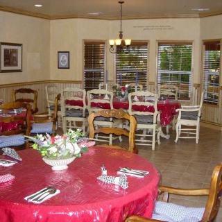 A cozy dining room with multiple tables covered in red tablecloths, surrounded by chairs and lit by a chandelier.