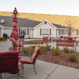 A cozy outdoor patio area with red cushioned furniture and an umbrella, set in front of a house.