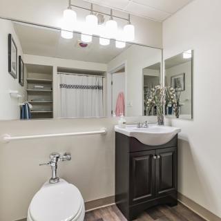 A modern bathroom with a sink, toilet, and large mirror, featuring bright lighting fixtures.