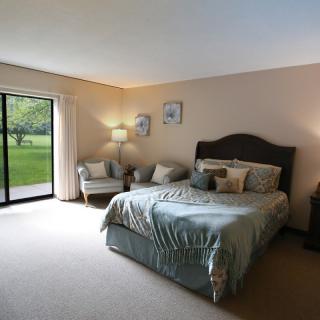 A cozy bedroom with a large bed, two chairs, lamps, and a sliding door leading to an outdoor view.