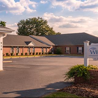 A view of a brick building with a sign and parking lot under a partly cloudy sky.