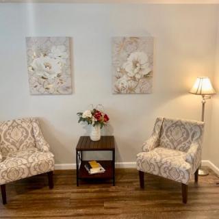 A cozy seating area with two patterned chairs, floral artwork, and a side table with flowers.