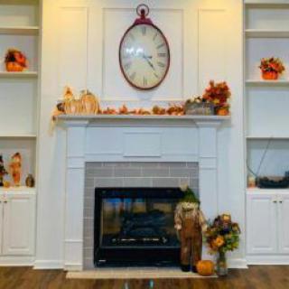 A cozy fireplace with autumn-themed decorations and a large clock above the mantel.