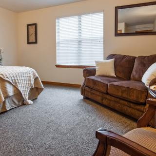 A cozy bedroom with a bed, a sofa, and a window letting in natural light.