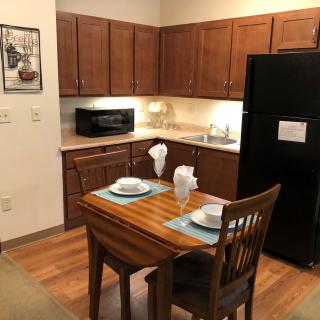 Cozy kitchen with a small dining table set for two, featuring wooden cabinets and a black refrigerator.