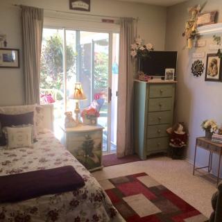 A cozy bedroom with floral bedding, a small dresser, and a view of the garden through sliding glass doors.