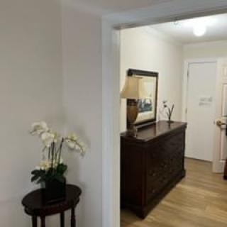 A view of a hallway with decorative furniture, a lamp, a painting, and an orchid on a small table.