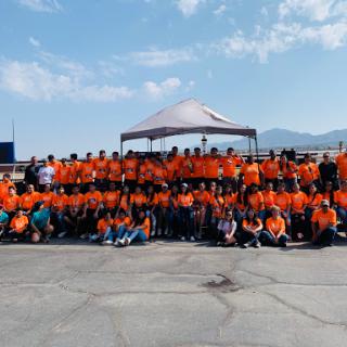 A vibrant gathering of team members united in orange shirts, enjoying a sunny day outdoors.