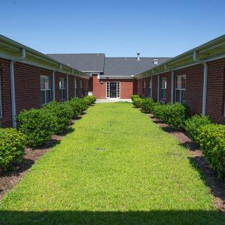 A symmetrical courtyard flanked by brick buildings with neatly trimmed grass and shrubs.