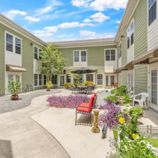 A charming courtyard with outdoor seating and colorful flowers nestled between residential buildings on a sunny day.