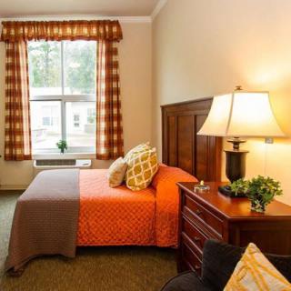 A cozy bedroom with a bed, nightstand, and lamp near a window with curtains.