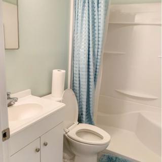 A small bathroom with a shower, toilet, and sink, featuring a light blue shower curtain and walls.