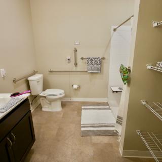 A clean and accessible bathroom with a shower, toilet, sink, and safety grab bars.