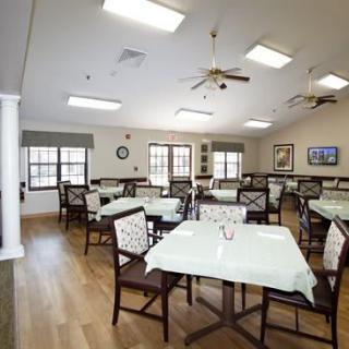 An empty dining room with neatly arranged tables and chairs, featuring wood flooring and ceiling fans.