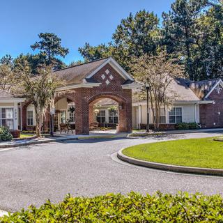 A building with a circular driveway and well-maintained landscaping, surrounded by trees under a clear blue sky.