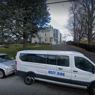 A van labeled 'Best Ride' parked on a street with trees and a large building in the background.