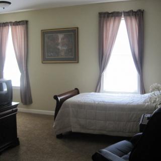 A cozy bedroom with a bed, television, and curtained windows.