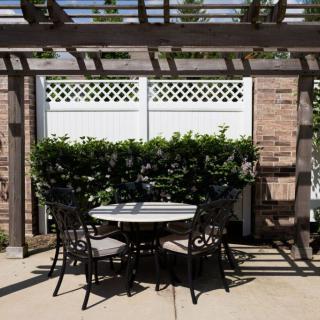 A patio area with a round table and four chairs under a pergola, surrounded by greenery.