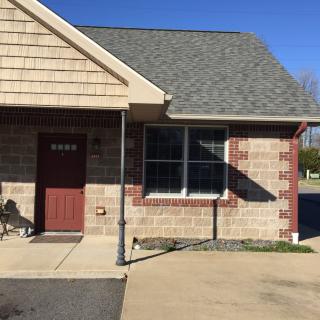 A small brick building with a red door and large window on a sunny day.