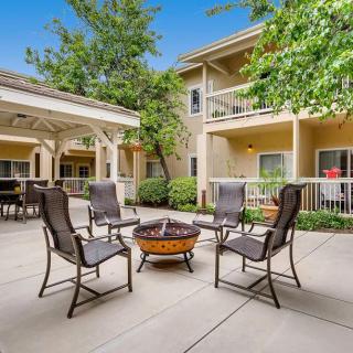 A cozy outdoor patio area with chairs arranged around a fire pit, surrounded by residential buildings and greenery.