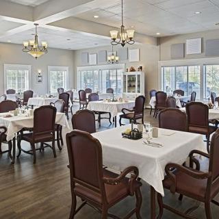 A spacious dining room with elegantly set tables and chairs, featuring large windows and chandeliers.