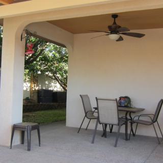 A cozy outdoor patio with a table, chairs, and a ceiling fan under a covered area.