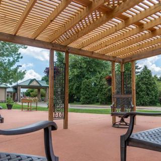 A patio with a wooden pergola and seating, offering a tranquil garden view on a sunny day.