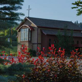 A serene view of a church surrounded by vibrant red flowers in a peaceful landscape.